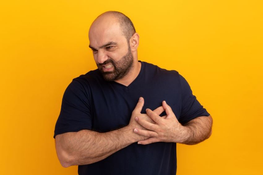 bearded-man-navy-t-shirt-holding-hands-chest-looking-unwell-standing-orange-wall.jpg