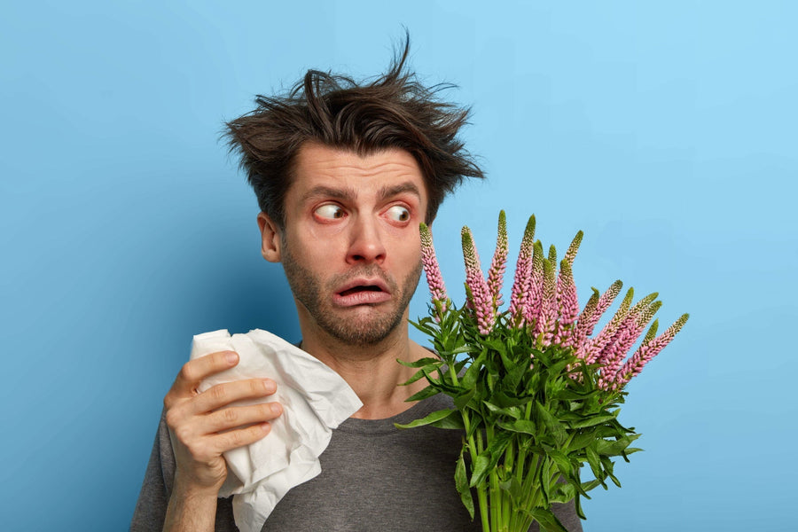 embarrassed-young-man-looks-surprisingly-plant-which-causes-allergy-holds-handkerchief-runny-nose-has-sensitive-immune-system-messy-hair-red-swelling-eyes-poses-against-blue-wall-min.jpg